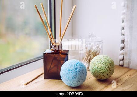 Badezimmer-Fensterbank aus Naturholz mit Flüssigdiffusor Flasche mit Holzstäben, natürliches Licht aus dem Fenster. Blaue und grüne beruhigende Badebomben. Stockfoto