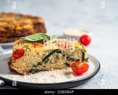 Zucchini Pie und Zutaten auf grauem Hintergrund, kopieren Raum. Stück köstliche herzhafte Torte mit Zucchini, Tomaten, Kräutern und Käse. Idee und Rezept Stockfoto