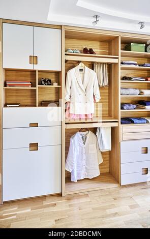 Interne Details der Holzgarderobe mit ausziehbarem Gestell für Kleiderständer. Moderner Kleiderschrank mit Kleidung, die auf ausziehbaren Racks hängt und auf dem gefaltet ist Stockfoto