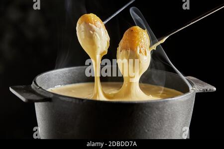 Köstliches, heiß dampfendes Schweizer Käsefondue mit gegrillten Babykartoffeln zum Eintauchen in die Nahaufnahme auf dunklem Hintergrund Stockfoto