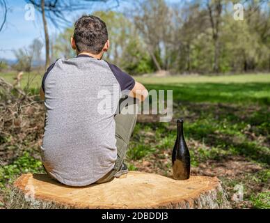 Ein unglücklicher Mann löst Probleme mit Alkohol. Traurig und allein mit einer Flasche Alkohol in der Natur. Stockfoto