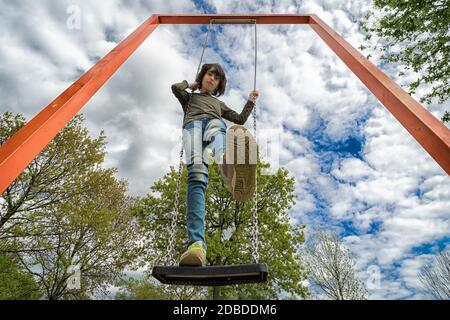 Ein Junge steht auf einer Schaukel. Blick von unten. Verzerrung eines Ultra-Weitwinkelobjektivs. Stockfoto