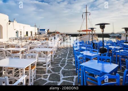 Café-Tische am Kai von Naousa Stadthafen in der berühmten Touristenattraktion Paros Insel, Griechenland bei Sonnenaufgang Stockfoto