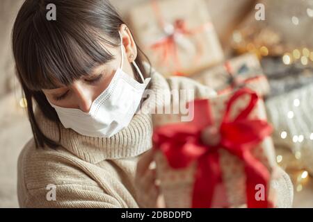 Junge Frau hält ein wunderschön eingewickeltes weihnachtsgeschenk. Konzept der Weihnachtsfeier während der Coronavirus-Pandemie. Stockfoto