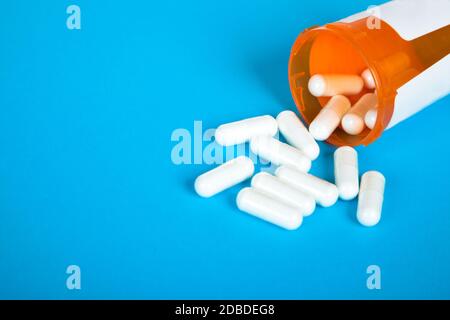 Weiße Pillen, die aus einer gestürzten leuchtend roten orangen Pillenflasche auf blauem Hintergrund auslaufen. Stock Foto Stockfoto