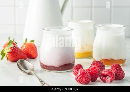 Weißer fruchtiger Joghurt im Glas und Himbeeren auf weißem Tisch. Stockfoto