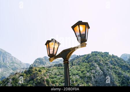 Glühende Straßenlampe vor dem Hintergrund von Bergen und Himmel Nahaufnahme. Stockfoto