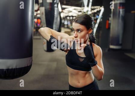 Frau in schwarzen Bandagen und Sportswear trifft einen Boxsack, thai Boxtraining. Boxerin in der Turnhalle, Mädchen Kämpfer im Sportverein, Ellbogenschläge pract Stockfoto