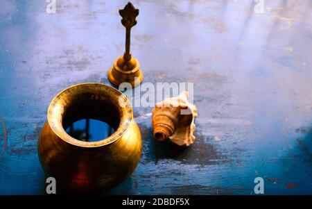 Close up Stillleben von antiken Holi Wassertopf und Glocke und Muschel auf rustikalem Boden. Glaube, Tradition, Spiritualität, Gebet, Symbole des Friedens und R Stockfoto