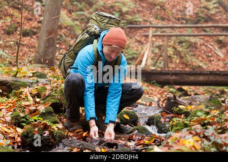 Backpacker schöpfen im Herbst Wasser aus einem Bergbach - Fokus auf das Gesicht Stockfoto