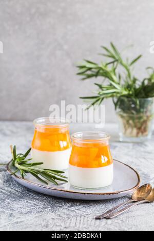 Hausgemachte Panna Cotta mit Scheiben von Pfirsich und Pfirsich Gelee in Glasgefäßen auf einem grauen Beton Hintergrund. Stockfoto