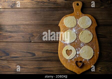 Herzförmige Knödel, Mehl auf Holzgrund. Kochknödel. Draufsicht mit Freiraum. Stockfoto