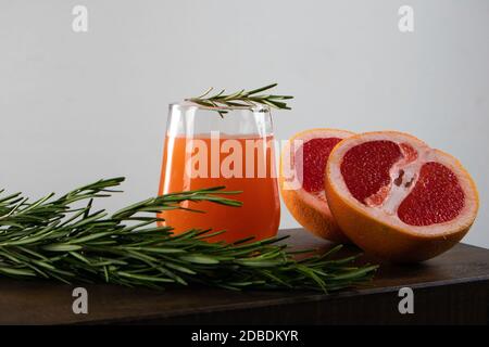Zwei Hälften aus roter Orange, Rosmarinzweig und ein Glas Orangensaft liegen auf einem Holztisch vor hellem Hintergrund Stockfoto