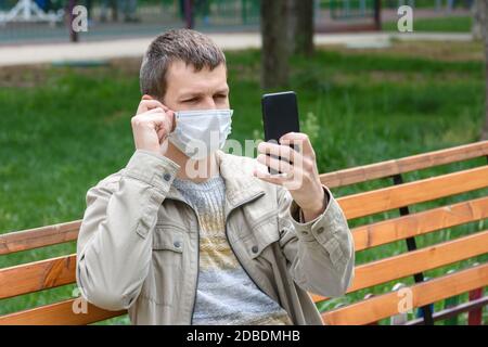 Ein Mann in einer medizinischen Maske sitzt auf einer Bank und passt die Maske an Stockfoto