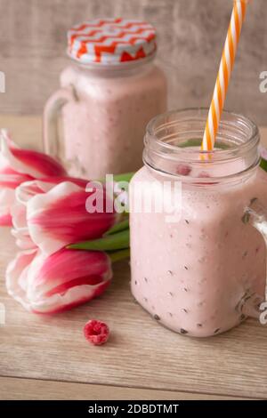 Pink Himbeer-Creme Smoothie in Einmachglas und Tulpen, vertikal Stockfoto