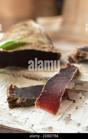 Wildsteak in Scheiben geschnitten, trockenes Fleisch von Wildrogen auf rustikalem Holzbrett, vertikale Abbildung Stockfoto