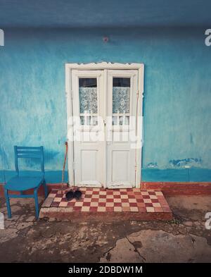 Holzkrücke und ein Paar alte Schuhe auf der Schwelle, vor der Tür des rustikalen Hauses. Traditionelle ländliche Gebäudefassade in Moldawien. Blau-lime lackiert Wal Stockfoto