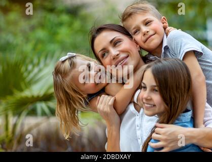 Porträt einer netten jungen Mutter mit Freude Zeit mit ihren drei kostbaren Kindern im Frühlingspark verbringen, jeder umarmen ihre schöne Mutter, mit Stockfoto