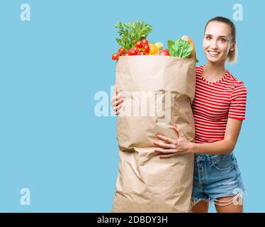 Fröhliche Frau hält eine riesige Einkaufstasche mit frischem Gemüse gefüllt, sie lächelt an der Kamera Stockfoto