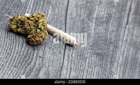 Eine volle Knospe von hochwertigem medizinischem Marihuana sitzt auf einem Holztisch mit einem gerollten Gelenk im Hintergrund. Stockfoto