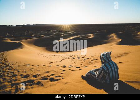 Arabische Person mit schwarz-weißen Jellaba sitzen in der Sand sieht die sahara Wüste und ein nahes Lager Stockfoto