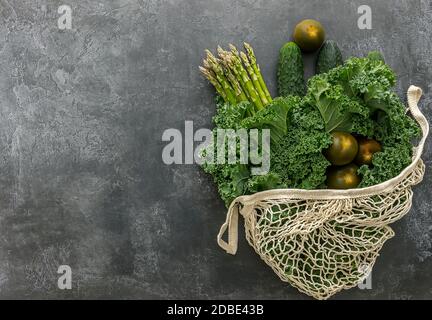 Grünes Gemüse im Saitenbeutel auf dunklem Hintergrund. Spargel, Broccolini, Grünkohl, Gurke, Avocado und Tomaten. Kein Plastikeinkaufskonzept. Stockfoto