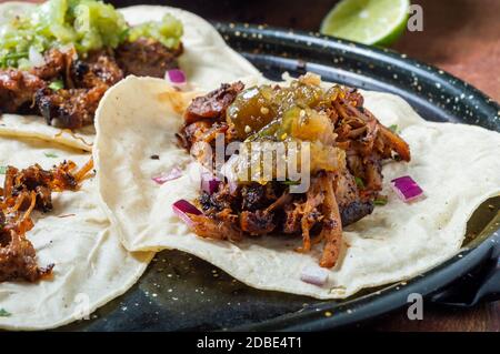 Carnitas Tacos mit roten Zwiebeln und roher Salsa verde. Mexikanische langsam gekochte Schweinefleisch Gericht aus Michoacan mit frischen grünen Salsa Stockfoto