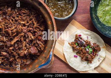 Carnitas Tacos mit roten Zwiebeln und roher Salsa verde. Mexikanische langsam gekochte Schweinefleisch Gericht aus Michoacan mit frischen grünen Salsa Stockfoto