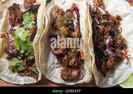 Carnitas Tacos mit roten Zwiebeln und roher Salsa verde. Mexikanische langsam gekochte Schweinefleisch Gericht aus Michoacan mit frischen grünen Salsa Stockfoto