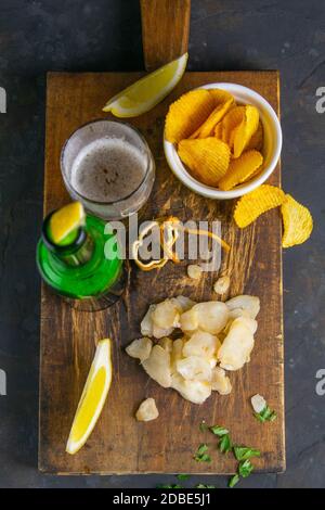 Getrockneter Oktopus mit Bier, Zitrone und Kartoffelchips auf dunklem Holzbrett. Snack auf Fisch mit Bier. Nahaufnahme. Stockfoto
