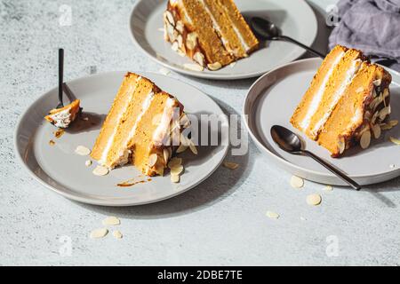 Flache Lage von Stücken veganer Kuchen auf einem grauen Teller. Hausgemachte Karottenkuchen mit weißer Sahne, Karamell und Nüssen. Stockfoto