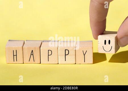 Holzwürfel mit dem Wort Happy auf hellgelbem Hintergrund, fröhliches Konzept Nahaufnahme Stockfoto