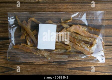 Getrocknete Karpfen Fisch Sticks in einer transparenten Verpackung mit einem weißen Etikett Vorspeise zu Bier auf Holzhintergrund. Snack Fisch zu Bier. Nahaufnahme. Stockfoto