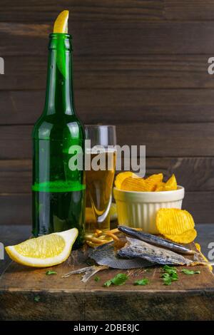 Getrocknete Brasse in Form eines Schmetterlings mit Bier, Zitrone und Kartoffelchips auf dunklem Holzbrett. Snack auf Fisch mit Bier. Nahaufnahme. Stockfoto