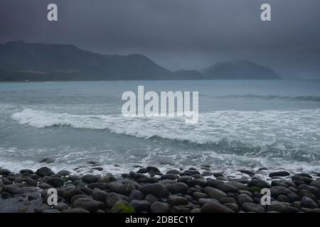 Regenwetter, türkisfarbenes Meer unter dunklen Wolken, Berge im Hintergrund. Neuseeland, Südinsel, in der Nähe von Kaikoura. Stockfoto