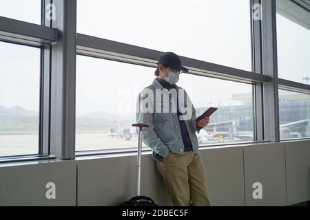 Junge asiatische Mann männliche Flugreisende Lesung e-Buch mit einem E-Reader beim Warten auf das Einsteigen im Flughafenterminal Stockfoto