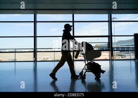 Silhouette eines asiatischen Mann männlichen Flugreisenden zu Fuß schieben Ein Wagen im Flughafengebäude Stockfoto