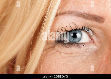 Nahaufnahme des rechten Auges einer blonden, blauäugigen Frau mittleren Alters. Stockfoto
