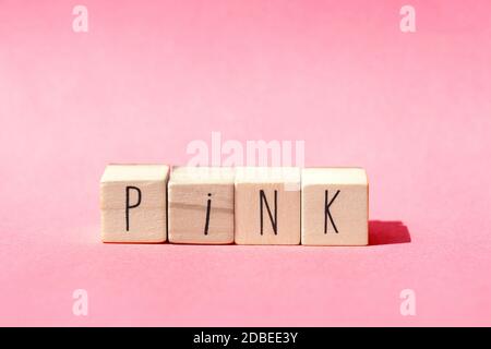 Holzwürfel liegen in einer Reihe auf rosa Hintergrund mit dem Wort Pink, Pastell rosa Natur Konzept close-up Stockfoto