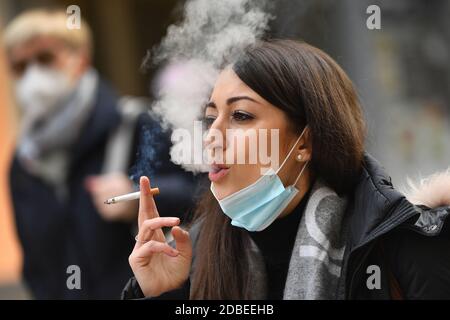 München, Deutschland. November 2020. Maskenpflicht in den Fußgängerzonen und öffentlichen Plätzen in München am 17. November 2020. Die junge Frau trägt ihre Alltagsmaske unter ihrem Gesicht und raucht eine Zigarette. MODELL FREIGEGEBEN! Quelle: dpa/Alamy Live News Stockfoto