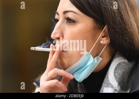 München, Deutschland. November 2020. Maskenpflicht in den Fußgängerzonen und öffentlichen Plätzen in München am 17. November 2020. Die junge Frau trägt ihre Alltagsmaske unter ihrem Gesicht und raucht eine Zigarette. MODELL FREIGEGEBEN! Quelle: dpa/Alamy Live News Stockfoto
