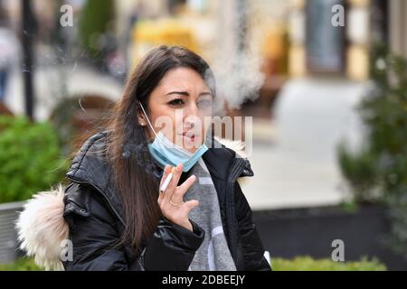 München, Deutschland. November 2020. Maskenpflicht in den Fußgängerzonen und öffentlichen Plätzen in München am 17. November 2020. Die junge Frau trägt ihre Alltagsmaske unter ihrem Gesicht und raucht eine Zigarette. MODELL FREIGEGEBEN! Quelle: dpa/Alamy Live News Stockfoto