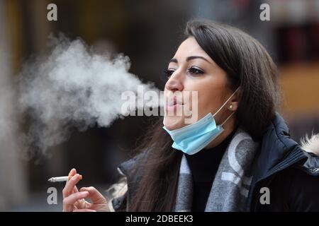 München, Deutschland. November 2020. Maskenpflicht in den Fußgängerzonen und öffentlichen Plätzen in München am 17. November 2020. Die junge Frau trägt ihre Alltagsmaske unter ihrem Gesicht und raucht eine Zigarette. MODELL FREIGEGEBEN! Quelle: dpa/Alamy Live News Stockfoto