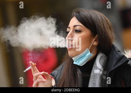 München, Deutschland. November 2020. Maskenpflicht in den Fußgängerzonen und öffentlichen Plätzen in München am 17. November 2020. Die junge Frau trägt ihre Alltagsmaske unter ihrem Gesicht und raucht eine Zigarette. MODELL FREIGEGEBEN! Quelle: dpa/Alamy Live News Stockfoto
