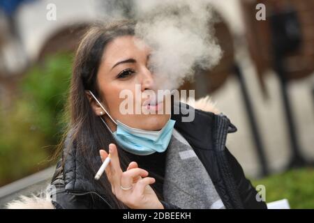 München, Deutschland. November 2020. Maskenpflicht in den Fußgängerzonen und öffentlichen Plätzen in München am 17. November 2020. Die junge Frau trägt ihre Alltagsmaske unter ihrem Gesicht und raucht eine Zigarette. MODELL FREIGEGEBEN! Quelle: dpa/Alamy Live News Stockfoto