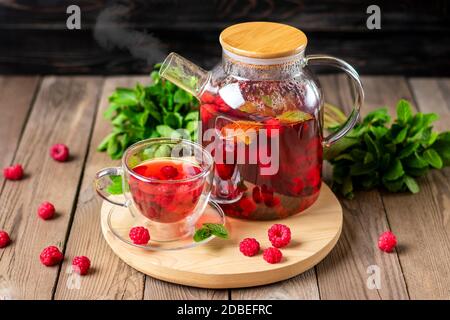 Kräutertee mit Beeren, Himbeeren, Minzblättern und Hibiskusblüten in Glas Teekanne und Tasse auf Holztisch Medizin für kaltes Vitamin Drink Rustikal Stockfoto