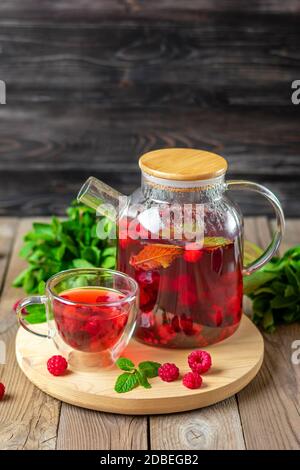 Kräutertee mit Beeren, Himbeeren, Minzblättern und Hibiskusblüten in Glas Teekanne und Tasse auf Holztisch Medizin für kaltes Vitamin Drink Rustikal Stockfoto