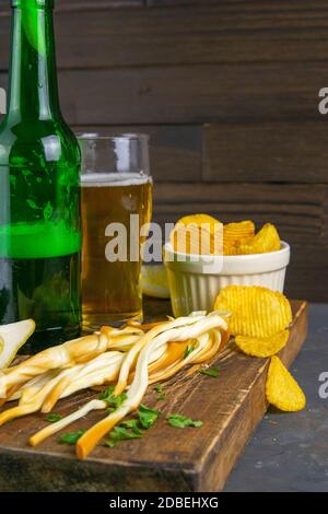 Käse mit Bier, Zitrone und Kartoffelchips auf dunklem Holzbrett. Snack auf Fisch mit Bier. Vorderansicht, Nahaufnahme. Stockfoto