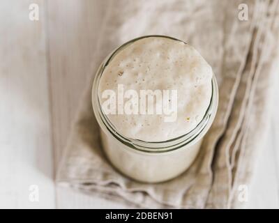 Weizensauerteig-Starter. Draufsicht des Glasgefäßes mit Sauerteig Starter auf weißem Holzhintergrund. Platz für Text oder Design kopieren. Stockfoto