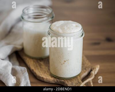 Zwei Gläser mit Vorspeisen aus Weizensauerteig in verschiedenen Hydratationsstufen. Starter 100 Prozent Hydratation im Vordergrund und Starter mit höherem hy Stockfoto